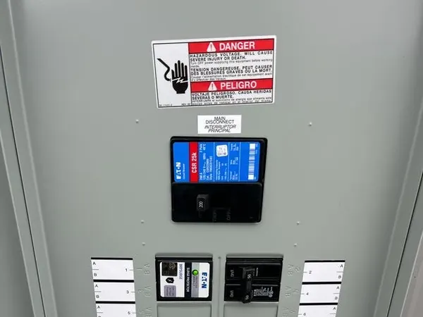 Open commercial panelboard with an Eaton main breaker and a labeled circuit directory on a corrugated metal wall.