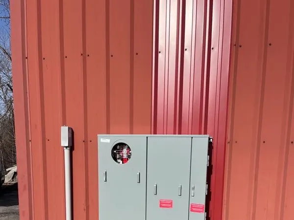 Gray commercial metering and gutter cabinets surface-mounted on a red corrugated-metal building with PVC riser conduit.