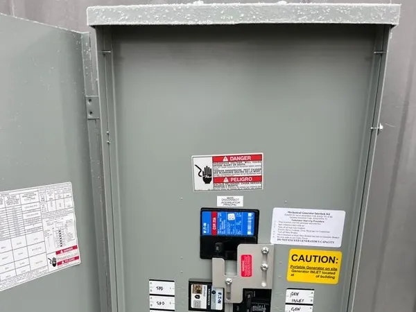 An open panelboard fitted with a generator interlock kit and generator-inlet labeling.