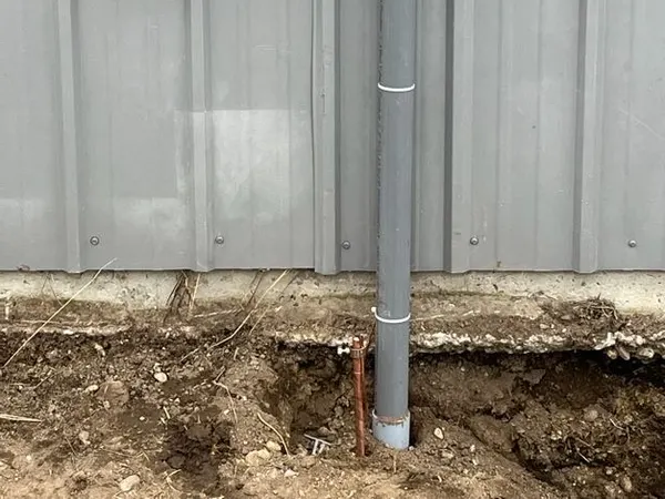 An exterior electrical enclosure and weatherproof receptacle on a metal building, with rigid conduit dropping into the ground.