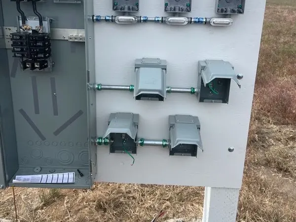 Open field-mounted service equipment with breakers and a board of metal boxes joined by rigid conduit.
