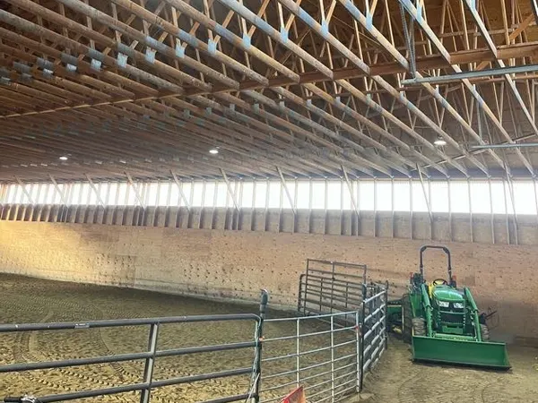 A pole-frame indoor arena with wood trusses and a lit high-bay fixture.