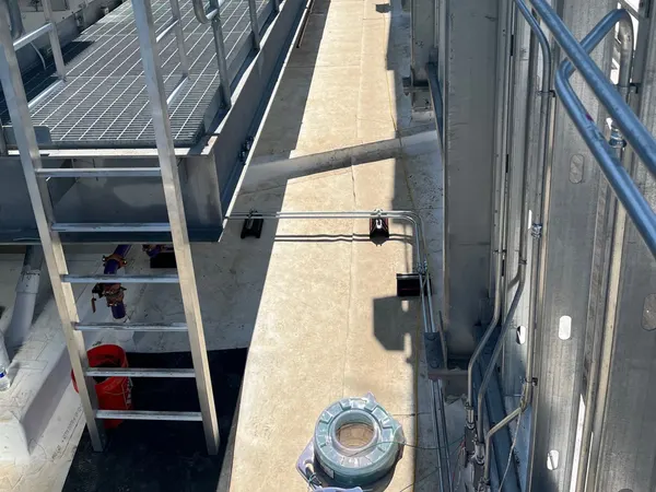 A long EMT conduit run along steel framing beside rooftop mechanical units and a catwalk on a commercial building.