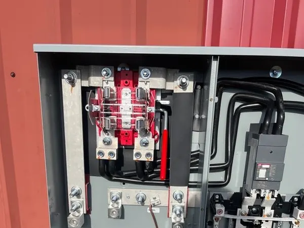 Open commercial service equipment showing heavy feeder lugs, a red current-transformer block, and a main breaker in a metal enclosure.