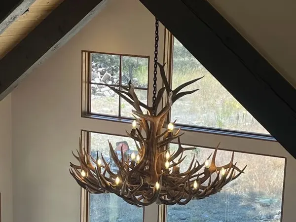 A large lit antler chandelier suspended in front of tall gable windows.