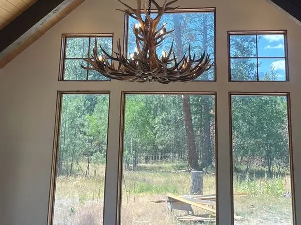 An antler chandelier and recessed lights in a vaulted beamed ceiling over forest-view windows.