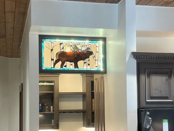 A backlit stained-glass elk transom over a butler pantry with under-cabinet lighting.
