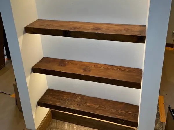 Wood floating shelves in a niche lit by concealed LED strip lighting.