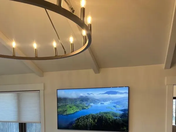 A living room with a large ring chandelier and a wall-mounted TV under a beamed ceiling.