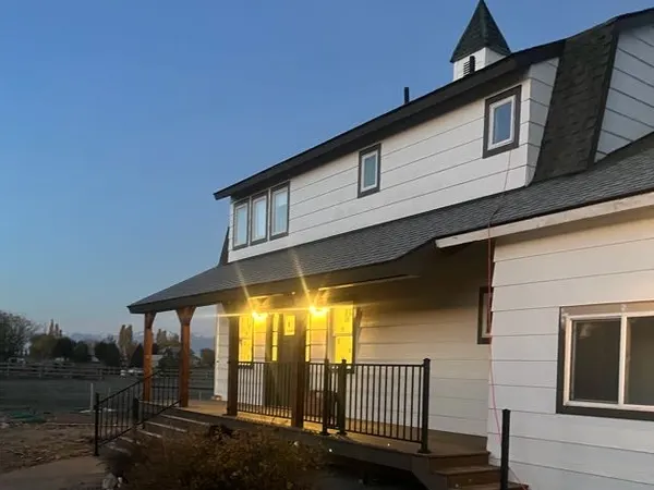 A two-story farmhouse at dusk with a lit porch and exterior soffit lights.