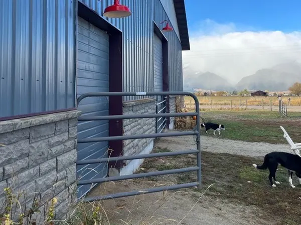 A metal barn exterior with two red gooseneck barn lights above the doorways.