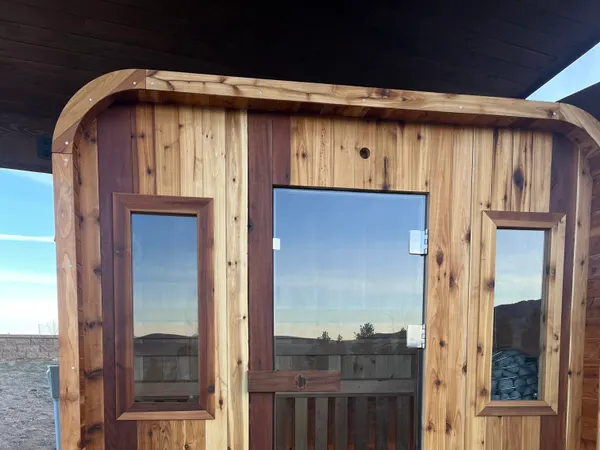 A finished cedar outdoor sauna with a glass door on a concrete patio.