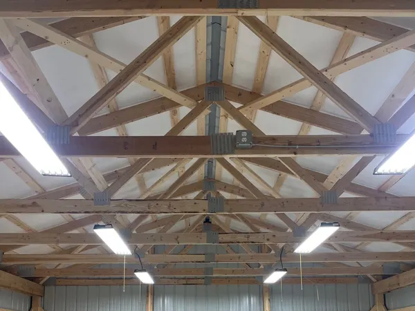 A wood-truss pole-building shop lit by a full grid of LED high-bay fixtures, with outlets on the posts and a workbench below.