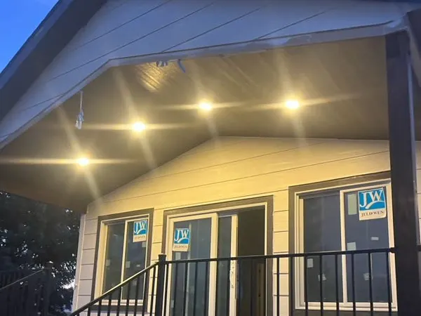 A row of recessed soffit lights glowing along the eave of a home at dusk, above a deck and railing.
