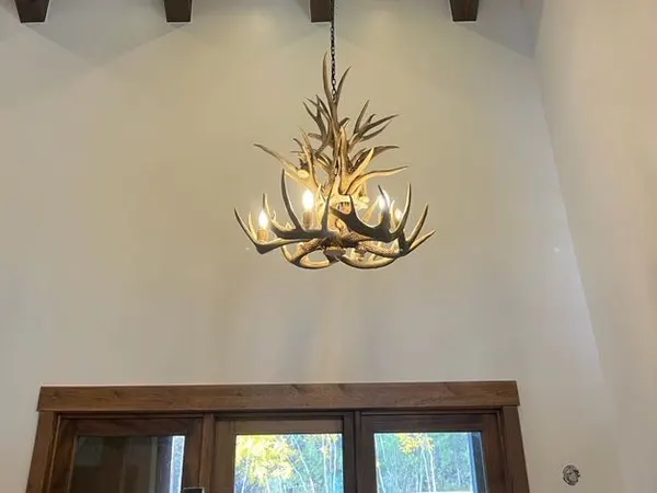 Recessed cans lit in a wood-plank ceiling with dark beams, above an antler chandelier in a two-story entry.