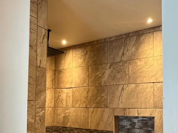 A tiled walk-in shower lit by a recessed ceiling light and a concealed LED accent niche.