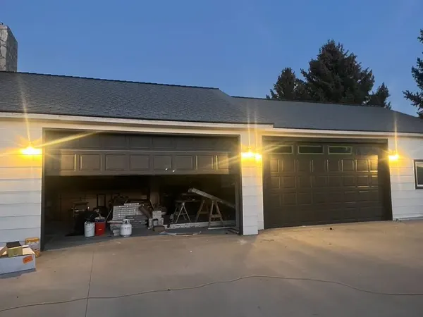 A three-bay garage at dusk with warm exterior coach lights lit between the doors.
