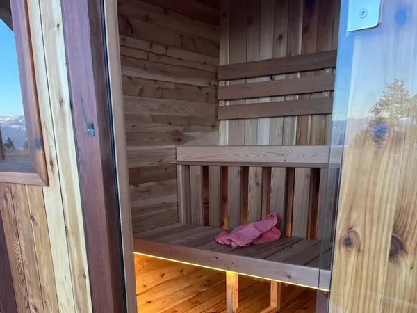 The cedar-lined interior of an outdoor sauna, warmly lit, with the heater and bench in view.
