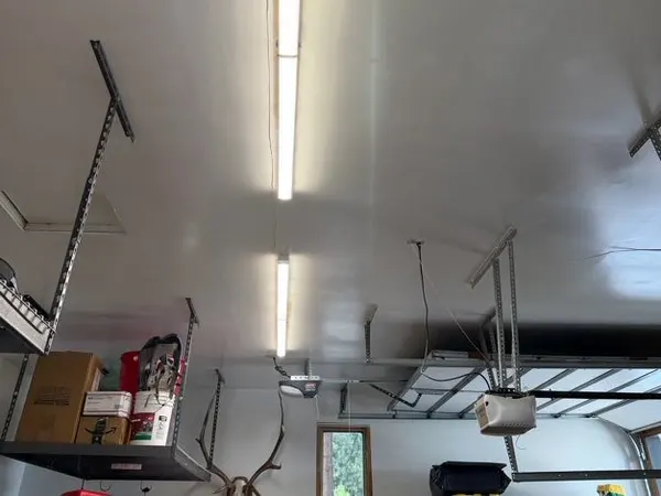 A long linear LED strip fixture lit across a shop ceiling above an overhead door and opener rail.
