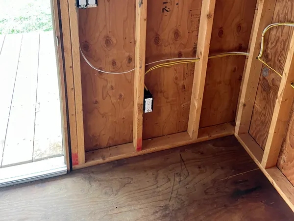 Rough-in switch and outlet boxes with white and yellow NM cable on a plywood-sheathed stud wall.
