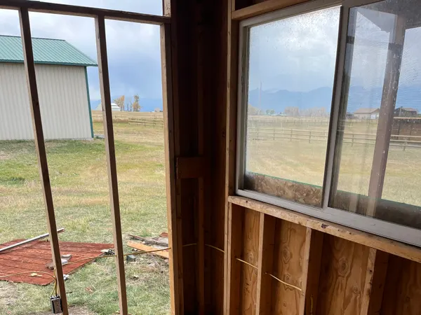 A rough-in outlet box on a framed wall beside windows overlooking a rural pasture.