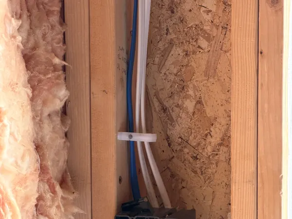 A rough-in metal device box with wire connections on a wood-stud wall beside fiberglass insulation.