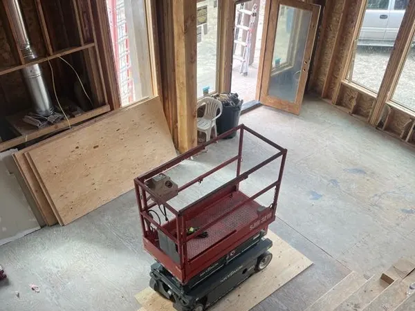 A red scissor lift on the subfloor inside a framed multi-level home under construction.