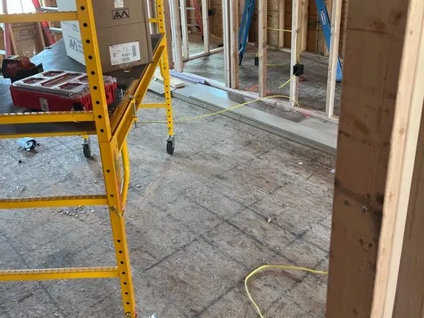 A rolling scaffold and ladders inside a framed house with electrical rough-in along the stud walls.