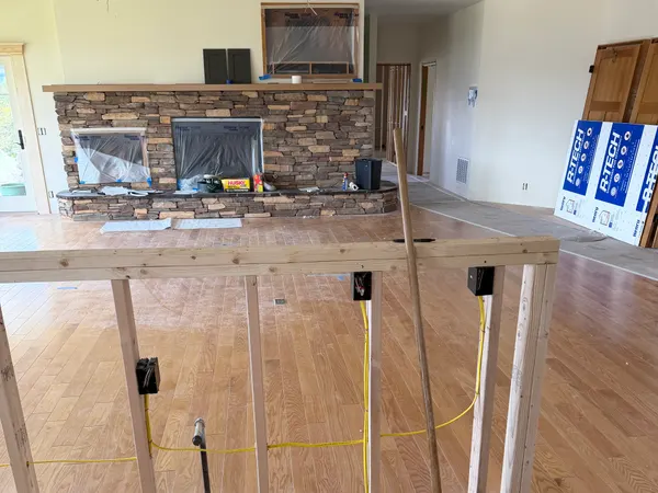 A great room mid-remodel with a newly framed half-wall holding rough-in boxes near a stone fireplace.