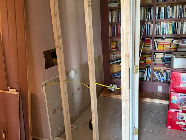 A home library being remodeled, with a new stud wall and cable run beside a full bookshelf.