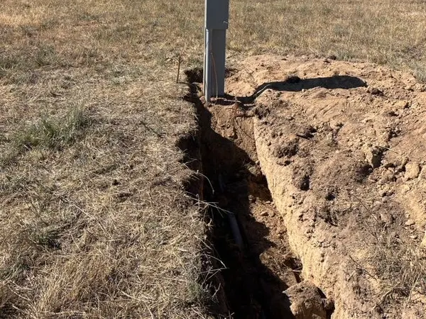A meter pedestal set at the head of an open trench in a Montana pasture, with fence line and mountains beyond.