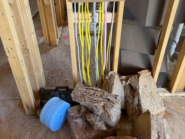 A bundle of yellow and white NM cables dropped down a framed chase to a rough-in box during a home wiring job.