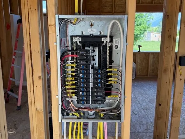 A rough-in residential load center in framing with many labeled circuits and cables entering top and bottom.
