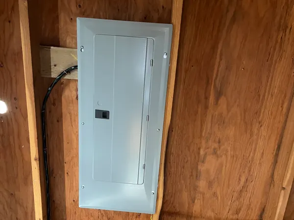 A residential breaker panel surface-mounted on a plywood-and-stud garage wall with a service-entrance feed.