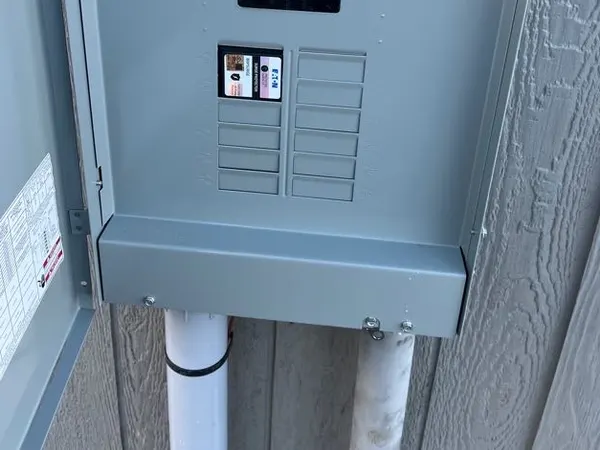 A closed exterior Eaton breaker panel fed by PVC conduit on gray house siding.