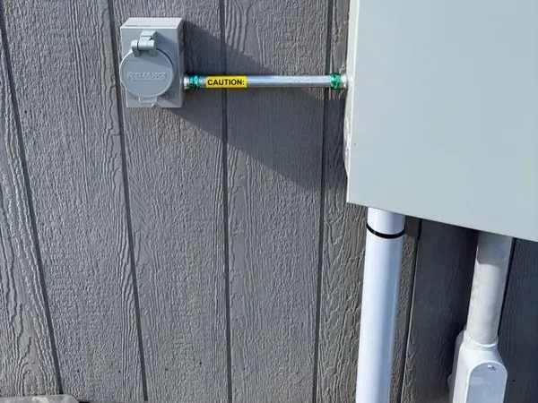 A generator power-inlet box connected by conduit to an emergency-disconnect enclosure on home siding.