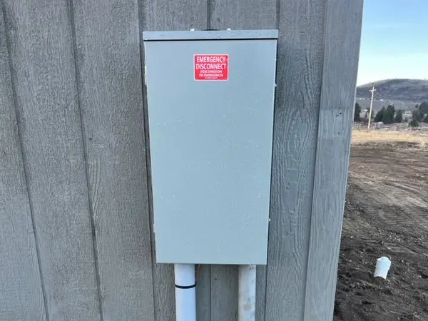 A meter-main with an emergency-disconnect label and a PVC service riser mounted on the board-and-batten siding of a new home.