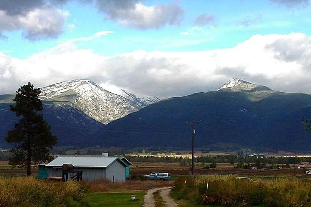 A farm outbuilding and gravel drive on the Bitterroot Valley floor with the snow-covered Bitterroot Mountains rising behind.